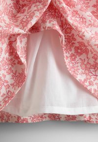 Rosa Blumenstoff, zurückgefaltet, um das darunter liegende glatte weiße Futter mit sichtbaren Nähten am Rand zu zeigen.