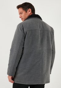 Abrigo de lana gris con cuello de piel sintética negra, diseño estructurado, mangas largas y corte recto. Detalles de costuras visibles en la parte trasera.