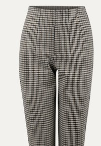 Kostkované kalhoty s černo-bílým vzorem houndstooth, plochým předním dílem a zužujícími se nohavicemi, vyrobené z texturované látky.