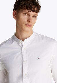 Camicia bianca con bottoni, colletto alla coreana e piccolo logo ricamato sul petto a sinistra. Realizzata in morbido cotone.