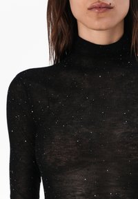 Svart, tettsittende turtleneck-top laget av gjennomsiktig stoff, med et spredt mønster av små, blanke paljetter over overflaten.