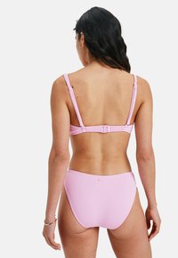 Rozā ribota bikinī komplekts ar regulējamiem siksnām, aizdari aizmugurē un augsto vidukli ar gludu tekstūru.