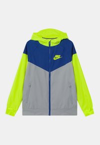 Giacca windbreaker Nike con cappuccio. Presenta un design a blocchi di colore in blu navy, giallo brillante e grigio. Materiale leggero con tasche con zip.