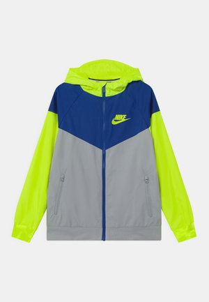 Kurtka Nike z kapturem typu wiatrówka. Posiada kolorowy design w granatowym, jaskrawożółtym i szarym kolorze. Wykonana z lekkiego materiału z zamykanymi na zamek kieszeniami.