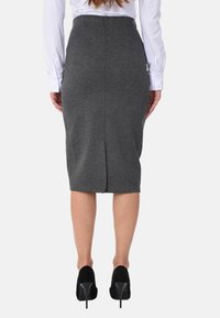 Gonna grigia a matita con uno spacco sul retro, realizzata in un materiale strutturato e aderente. Abbinata a scarpe con tacco alto nere e una camicia bianca a maniche lunghe.
