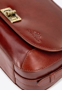 Borsa in pelle marrone con chiusura in ottone, dettagli cuciti e logo impresso. Texture liscia con una forma strutturata e design elegante.