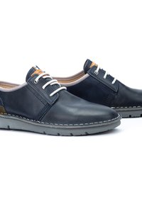 Scarpe in pelle blu navy con lacci bianchi e accenti marroni a contrasto. Punta arrotondata, suola in gomma grigia e dettagli di cucitura visibili.