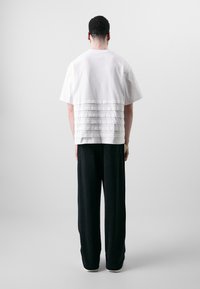 White short-sleeve shirt with horizontal pleats at the back, paired with black wide-leg trousers, worn by a person from the back.
