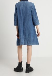 Jeansklänning, midjehöjd, trekvartslånga ärmar, lös passform, mörkblå färg, mitt bak med sömdetalj, tillsammans med svarta ankelboots.