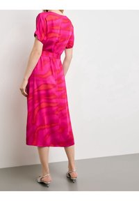 Różowa midi sukienka z gładkiego materiału, z falistym pomarańczowym wzorem, krótkimi rękawami, dopasowaną talią i rozkloszowanym dołem.