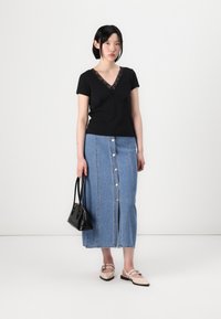 Svart kortermet topp med blondekant, sammen med et lyst denimskjørt med forklaring og slisse, komplementert av en svart veske og lyse sko.