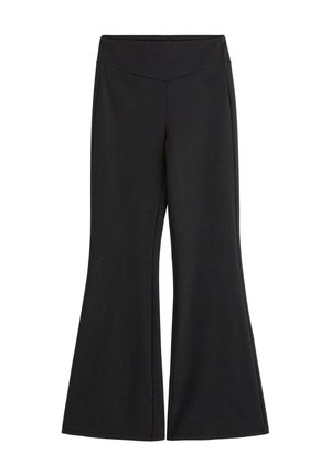 Femme debout pieds nus sur un fond beige, vêtue d'un crop top rose pâle sans manches et d’un pantalon flare noir taille haute.
