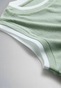 Pile de t-shirts manches courtes à col rond, pliés, en vert clair et blanc sur une surface neutre.