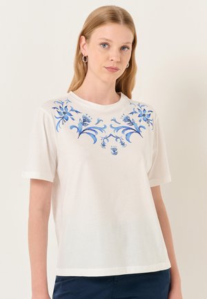 T-shirt blanc à manches courtes, avec une broderie florale bleue sur la poitrine, col rond et coupe décontractée. Texture de tissu douce.