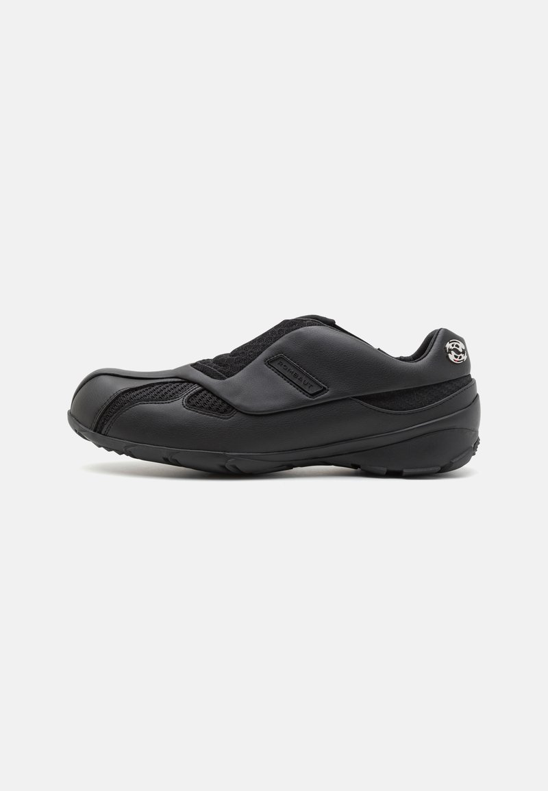 Des chaussures de sport noires avec une combinaison de cuir lisse et de tissu en maille, dotées d'une sangle à boucle et d'un design de semelle structurée.