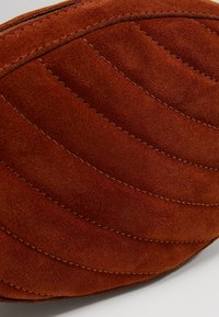 Gros plan d'un matériau en suède marron avec des lignes courbes cousues et matelassées, montrant une texture douce et un savoir-faire détaillé.