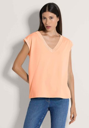 Pfirsichfarbener Kurzarmtop mit V-Ausschnitt-Design aus leichtem Stoff. Glatte Textur und entspannte Passform, kombiniert mit blauem Denim.