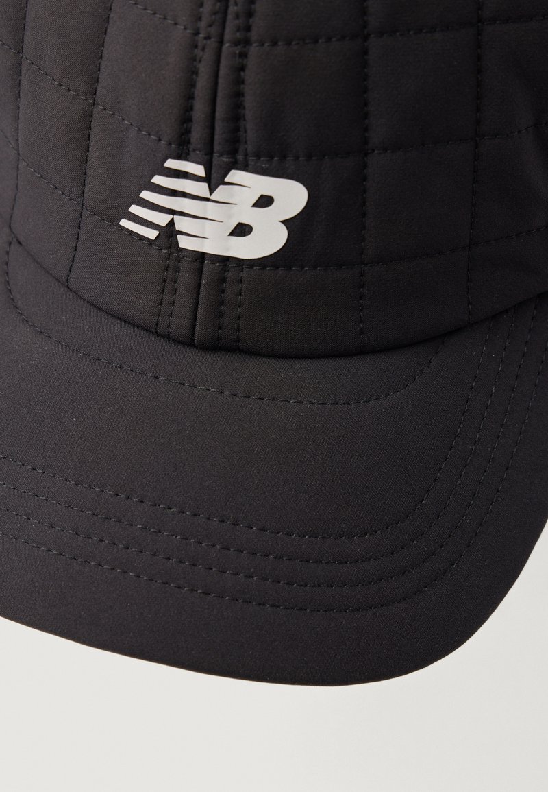 Gorra negra hecha de tela acolchada, con visera curvada y un prominente logo blanco "NB" en el frente. Textura suave con detalles cosidos.