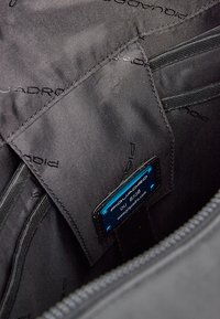 Black nylon interior with subtle logo pattern, featuring a blue label with brand information and a zipper pocket for storage.