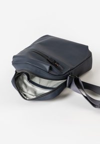 Marineblaue Leder-Crossbody-Tasche mit Reißverschluss, schlankem Profil und einem hellen Innenraum mit einer Seitentasche. Verstellbarer Trageriemen inklusive.