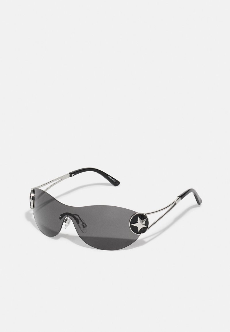 Saules brilles ar plānu, tumši pelēku lēcu, sudraba metāla rāmi un melnu zvaigznītes akcentu katrā pusē. Iekļauta mūsdienīga, izliekta forma.