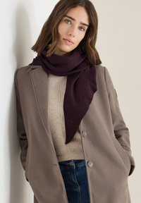 Écharpe bordeaux avec de petites éraflures, drapée élégamment, portée sur un pull beige et un manteau gris, présentant un look texturé et superposé.