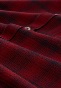 Czerwona i granatowa koszula flanelowa w kratę z zapięciem na guziki, o miękkiej fakturze i złożonym kołnierzyku, prezentująca wzór w kratkę.