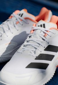 Λευκά αθλητικά παπούτσια με μαύρες ρίγες, από διχτυωτό ύφασμα και ροζ λεπτομέρειες. Διαθέτουν υφασμάτινη σόλα και επίπεδες κορδόνια για ασφαλή εφαρμογή.