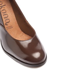 Chaussure en cuir verni marron avec un bout arrondi et un design découpé. La doublure intérieure présente un texte en relief "cuir véritable". Fini lisse et brillant.