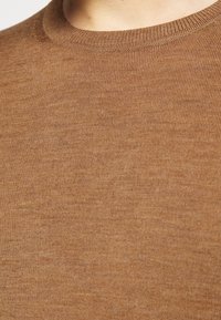 Gros plan sur un pull marron à col rond en tricot montrant la texture du tissu et les détails des coutures.