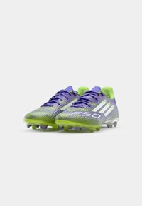Soccer cleats with a purple and green gradient, featuring textured synthetic material, white stripes, and a rounded toe design.