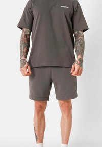 Grijze katoenen t-shirt met korte mouwen en een ronde hals, gecombineerd met bijpassende grijze shorts. Beiden hebben een relaxte pasvorm en een minimalistisch ontwerp.