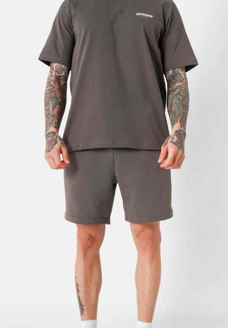 Grijze katoenen t-shirt met korte mouwen en een ronde hals, gecombineerd met bijpassende grijze shorts. Beiden hebben een relaxte pasvorm en een minimalistisch ontwerp.