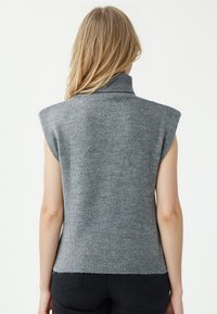 Grauer, gestrickter ärmelloser Pullover mit hohem Kragen und geripptem Saum, der eine weiche Textur und eine figurbetonte Silhouette aufweist.