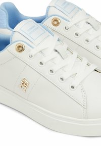 Baskets blanches en cuir synthétique lisse, avec des accents bleu clair, des lacets blancs, des détails dorés et un logo sur le côté.