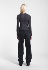 Top nero a maniche lunghe a costine con cuciture blu, abbinato a pantaloni neri larghi con due tasche posteriori e design a gamba dritta.