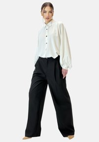 Blusa de satén blanca con collar y cierre de botones al frente, combinada con pantalones de pierna ancha negros de cintura alta. Ambas prendas presentan texturas suaves.