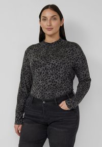 Bluzka z długim rękawem w szarym materiale z czarnym nadrukiem w panterkę, z wysokim kołnierzem i dopasowanym fasonem, zestawiona z czarnymi dżinsami.