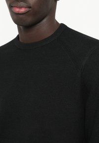 Fekete kötött pulóver kerek nyakkivágással, bordázott textúrával és raglán ujjakkal. Simák az anyagok, nincsenek látható minták vagy díszítések.