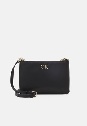 Czarna torba na ramię Calvin Klein z złotymi łańcuszkami, regulowanym paskiem i złotym logo CK na przodzie na białym tle.