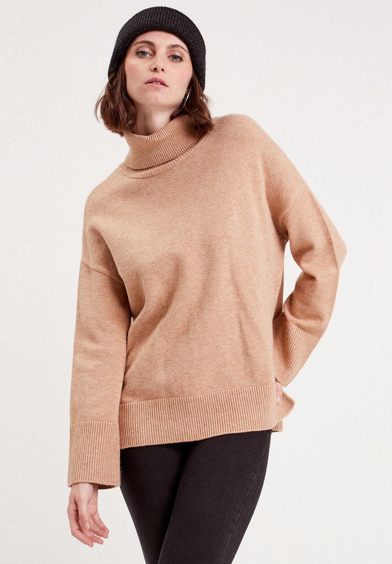 Un pull à col roulé surdimensionné en tissu doux, avec des poignets et un ourlet côtelés. Assorti à un jean sombre et à un bonnet en maille noir.