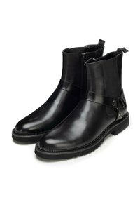 Botines de cuero negro con acabado liso, cremalleras laterales y una correa decorativa con detalles metálicos. Suelas gruesas de goma que ofrecen tracción.