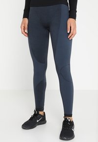 Námořnické legíny vyrobené z texturované, pružné látky s akcenty panelů. Mají přiléhavý design a jsou kombinovány s černými sportovními botami.