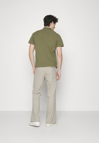 Olivengrønn polo skjorte med korte ermer, kombinert med beige rutete bukser; enkle hvite sneakers fullfører antrekket.