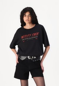 Must-valge lühikeste varrukatega t-särk punase "Mötley Crüe" graafikaga, millel on julged kirjatüübid ja välgudisain. Kantud studidega musta vööd ja šortse.