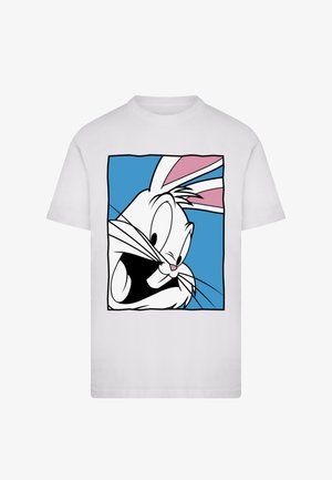 Wit T-shirt met het gezicht van een cartoonkonijn, met zwarte lijnen en een roze en blauwe achtergrond. Het konijn heeft grote expressieve ogen en snorharen.