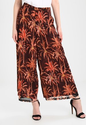 Wide-leg brown pants with orange palm tree print, worn with black high-heeled sandals and a white top.