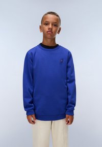 Felpa blu con polsini e colletto a coste. Presenta un piccolo logo sul petto. Abbinate a pantaloni di colore chiaro.
