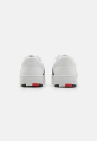 Adidași albi cu un finisaj din piele netedă, având accente albastre și roșii, un toc texturat și detalii de marcă pe talpă.