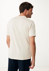 Krátký rukáv krémové tričko vyrobené z měkké, lehké tkaniny, s klasickým kulatým výstřihem, rovného lemu a minimálním švem.
